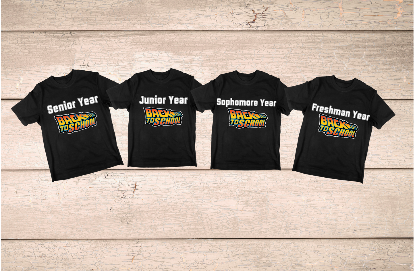 Four black t-shirts with different year labels on a wooden surface